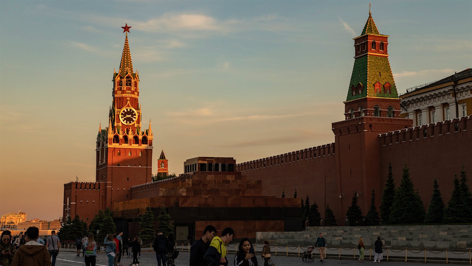 Exterior view of the Kremlin clock tower and wall from Red Square, with people walking in front of the building