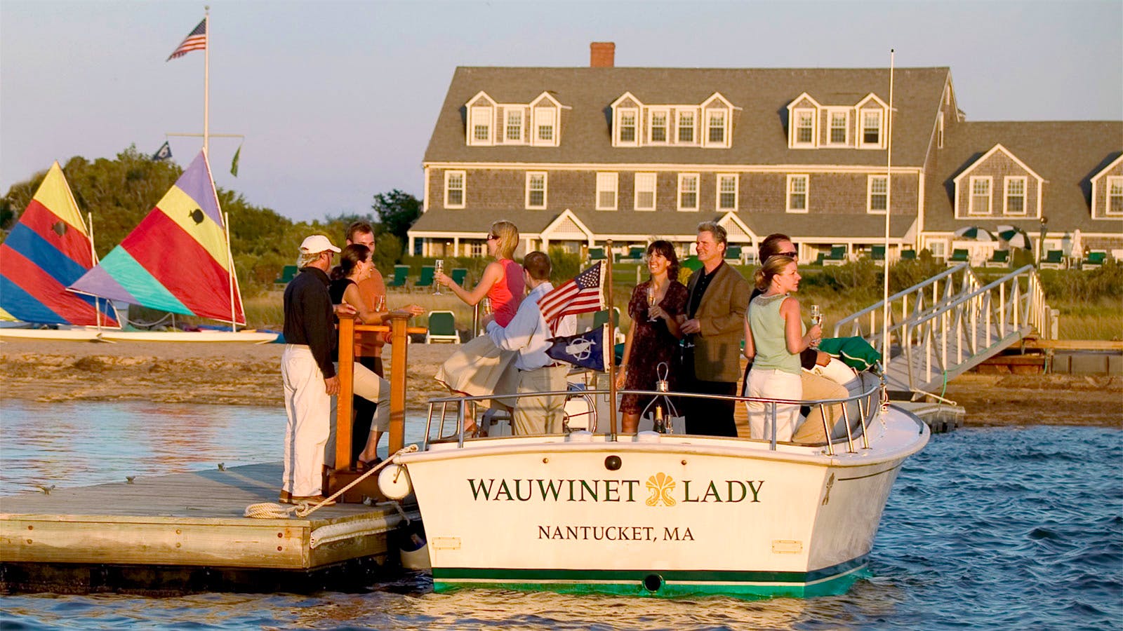 Guests holding glasses of wine and disembarking a boat named the "Wauwinet Lady" in front of the Wauwinet Inn on Nantucket